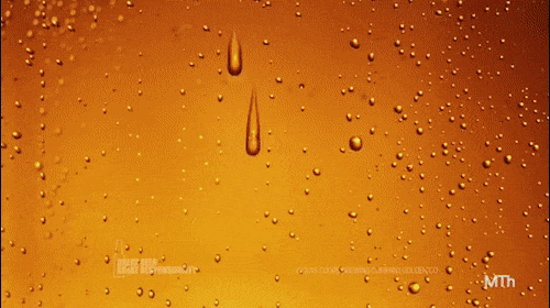 Close-up of condensation on a glass surface with golden-yellow liquid, featuring scattered water droplets and larger drips.