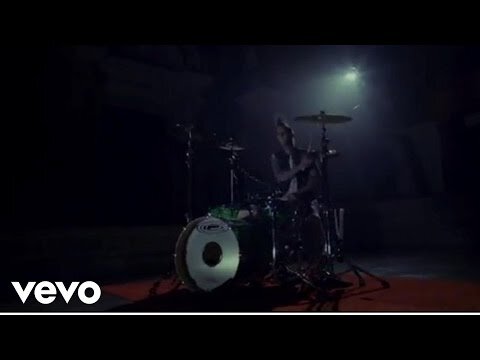 An adult drummer performing on a drum set in a dark environment with one spotlight on the performer and drum set, musical performance.
