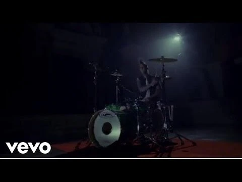 An adult drummer performing on a drum set in a dark environment with one spotlight on the performer and drum set, musical performance.