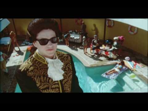 Adult male in period costume with sunglasses standing near a pool party with multiple people. Summer party with many people at the pool.