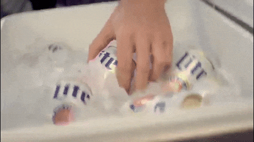 Close-up of a hand placing cans of Miller Lite beer on ice in a white basin, showcasing the brand and refreshing beverage.
