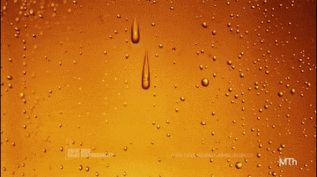 Amber beverage condensation drops on a glass surface with two prominent vertical droplets and visible warning label text.