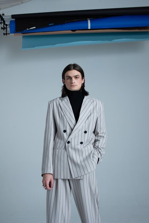 Fashionable young adult in a stylish striped suit poses confidently in a photo studio with diffused lighting, set against a neutral backdrop.