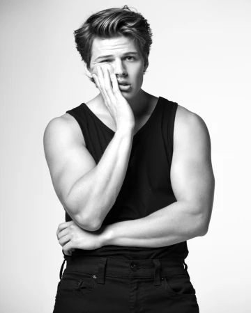 Portrait of a man in a black tank top holding his hand to his face against a white seamless background