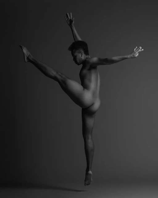 Monochrome artistic portrait of a bare-chested man in a dynamic dance pose against a dark background, showcasing strength and flexibility.