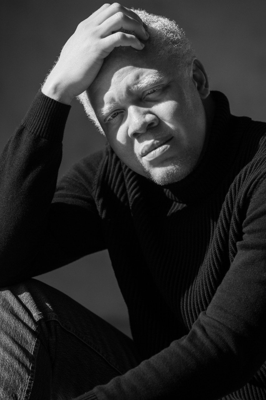 Close-up monochrome portrait of a Black man with white hair wearing a black turtleneck sweater, photographed by Parker Burr