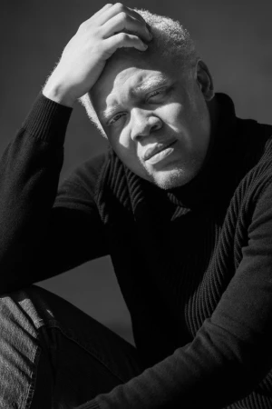 Close-up monochrome portrait of a Black man with white hair wearing a black turtleneck sweater, photographed by Parker Burr