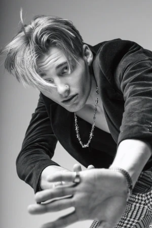 Monochrome portrait of a young man wearing a dark blazer and patterned trousers reaching toward the camera