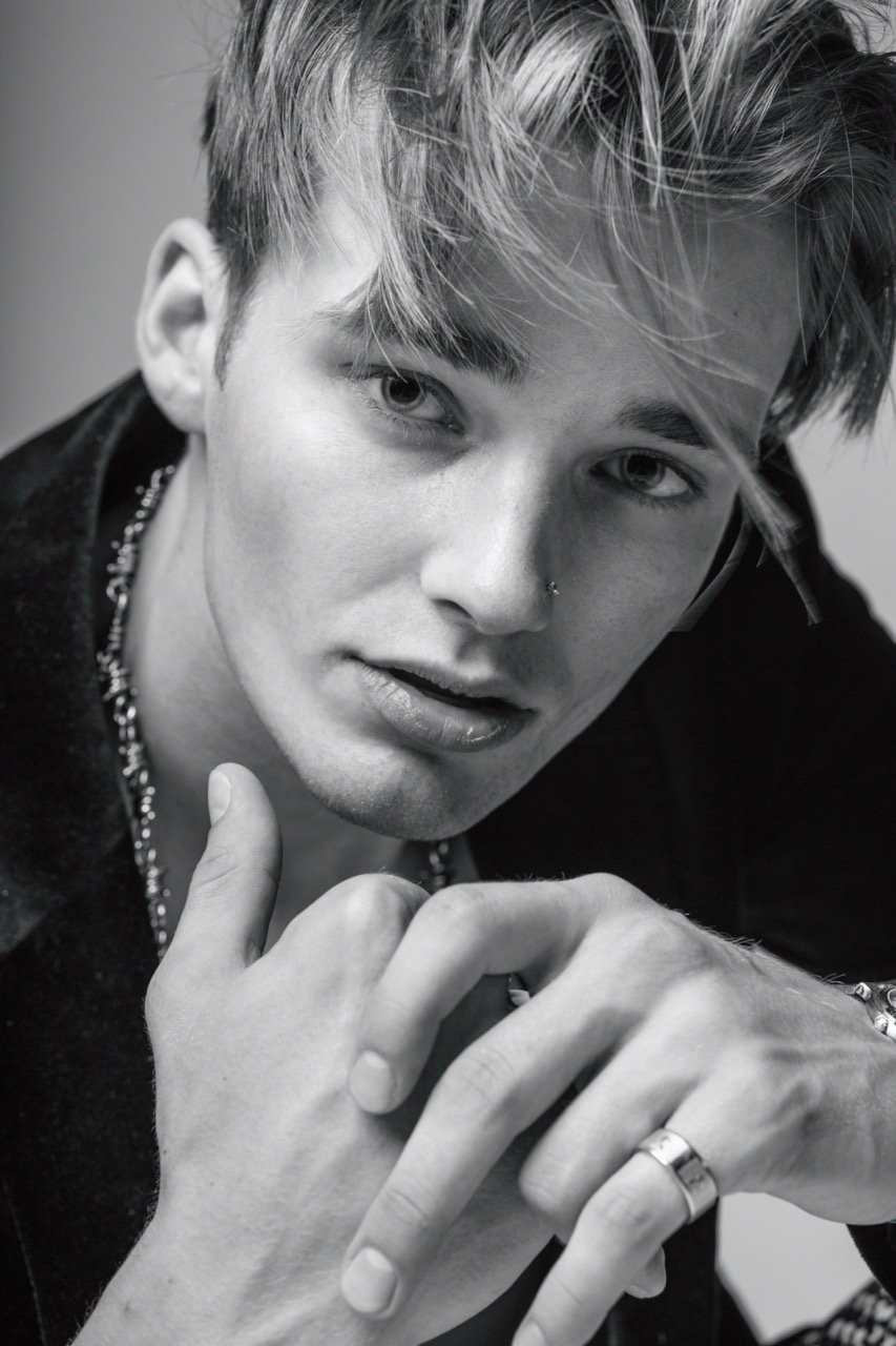 Close-up portrait of a young man with styled blond hair and nose ring wearing a dark shirt, photographed by Parker Burr.