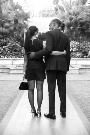 Black and white portrait from behind of a man and woman embracing outdoors near trees and a path by Parker Burr.
