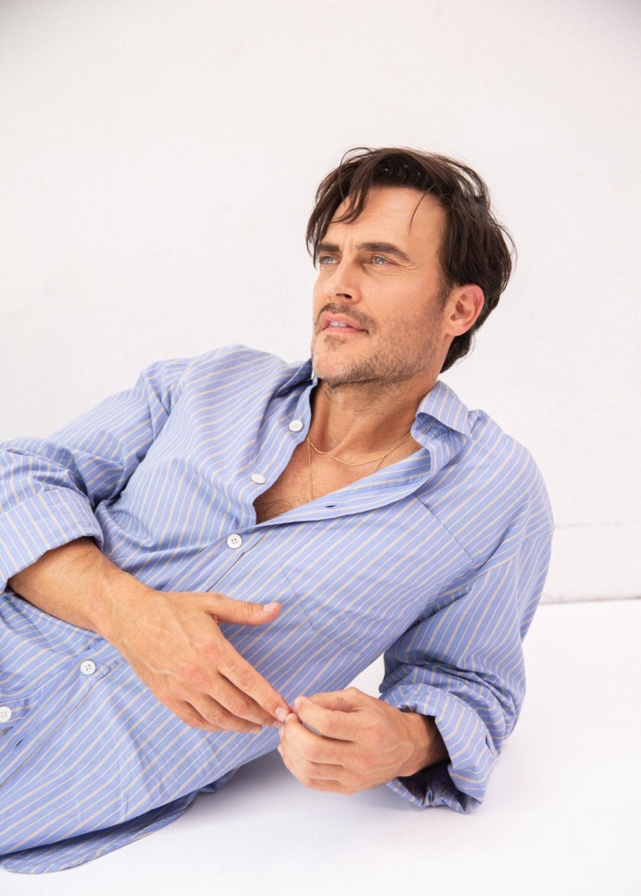 Man wearing a blue striped button-down shirt reclining against a bright white background