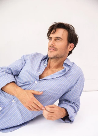 Man wearing a blue striped button-down shirt reclining against a bright white background