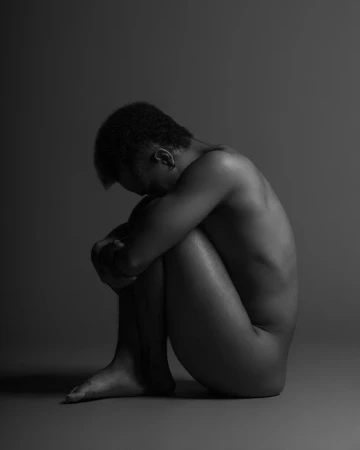Black and white portrait of a seated person curled in profile against a gradient studio background