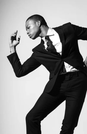 Black man in a tailored black suit and white shirt posing dynamically against a plain white background