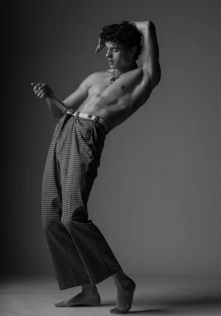 Shirtless man in patterned trousers posing against a grey studio backdrop by Parker Burr