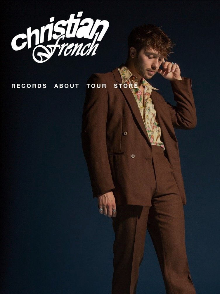 Man in a brown suit standing against a blue background, wearing a floral shirt with text overlay: Christian French Records About Tour Store.