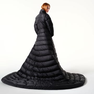 Rear shot of a woman wearing a full-length black puffer coat or dress against a bright white backdrop in a studio setting.