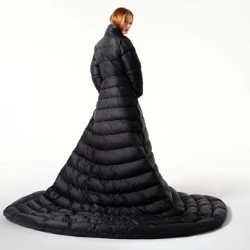 Rear shot of a woman wearing a full-length black puffer coat or dress against a bright white backdrop in a studio setting.