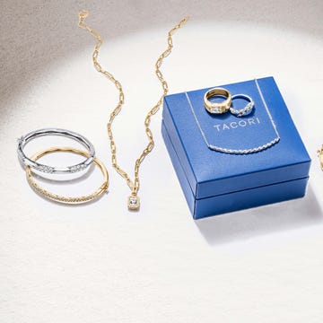 Close-up of fine jewelry, including gold chain necklace, gold and silver bangle bracelets, and a royal blue jewelry box with rings.