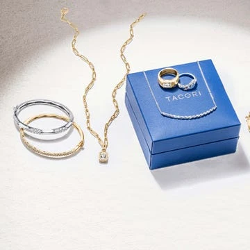 Close-up of fine jewelry, including gold chain necklace, gold and silver bangle bracelets, and a royal blue jewelry box with rings.