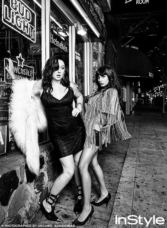 Black and white shot of two adult women posing outside a building at night with neon signs and wearing dresses and high heels.