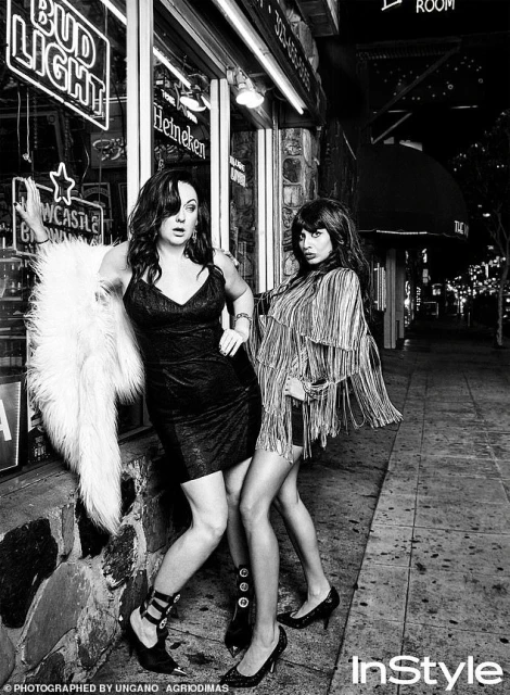 Black and white shot of two adult women posing outside a building at night with neon signs and wearing dresses and high heels.