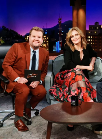 James Corden and Michelle Pfeiffer sitting on a couch in 'The Late Late Show' set with a cityscape backdrop at night.