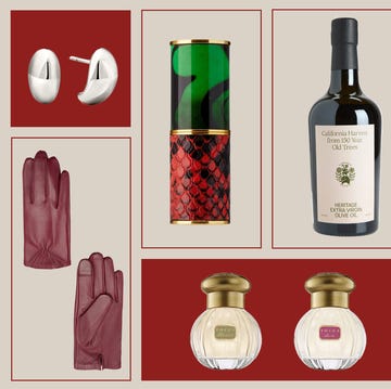 Product still life featuring beauty items, jewelry, leather gloves, and olive oil against a neutral and red color block background.