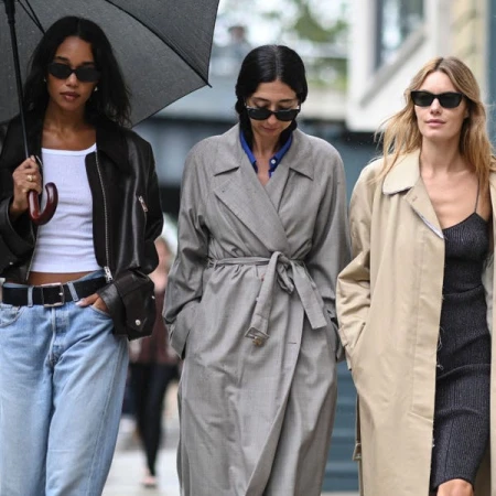 Three women walking down a city street, styled by Penny Lovell in coats and sunglasses.