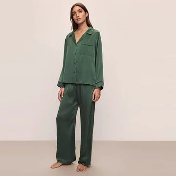 Adult female posing in full-length shot wearing emerald green silk pajamas indoors against a neutral wall in a fashion studio setting.