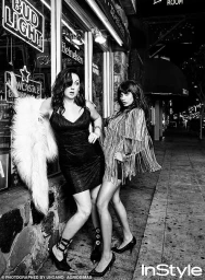 Two women posing on a city sidewalk at night outside a storefront, styled by Penny Lovell in a black-and-white photograph