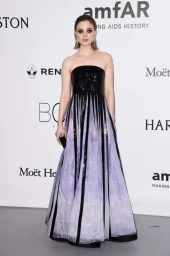 Woman wearing a strapless black and lavender sequin gown standing against a branded white step and repeat backdrop