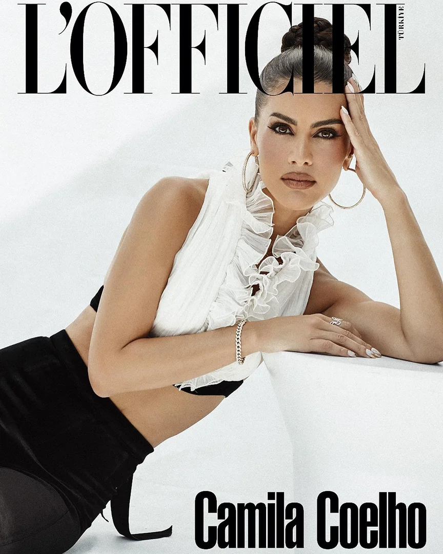 Camila Coelho in a ruffled white top and black skirt leaning against a white structure for L'Officiel, styled by Philippe Uter.