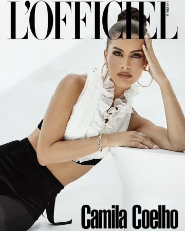 Camila Coelho in a ruffled white top and black skirt leaning against a white structure for L'Officiel, styled by Philippe Uter.