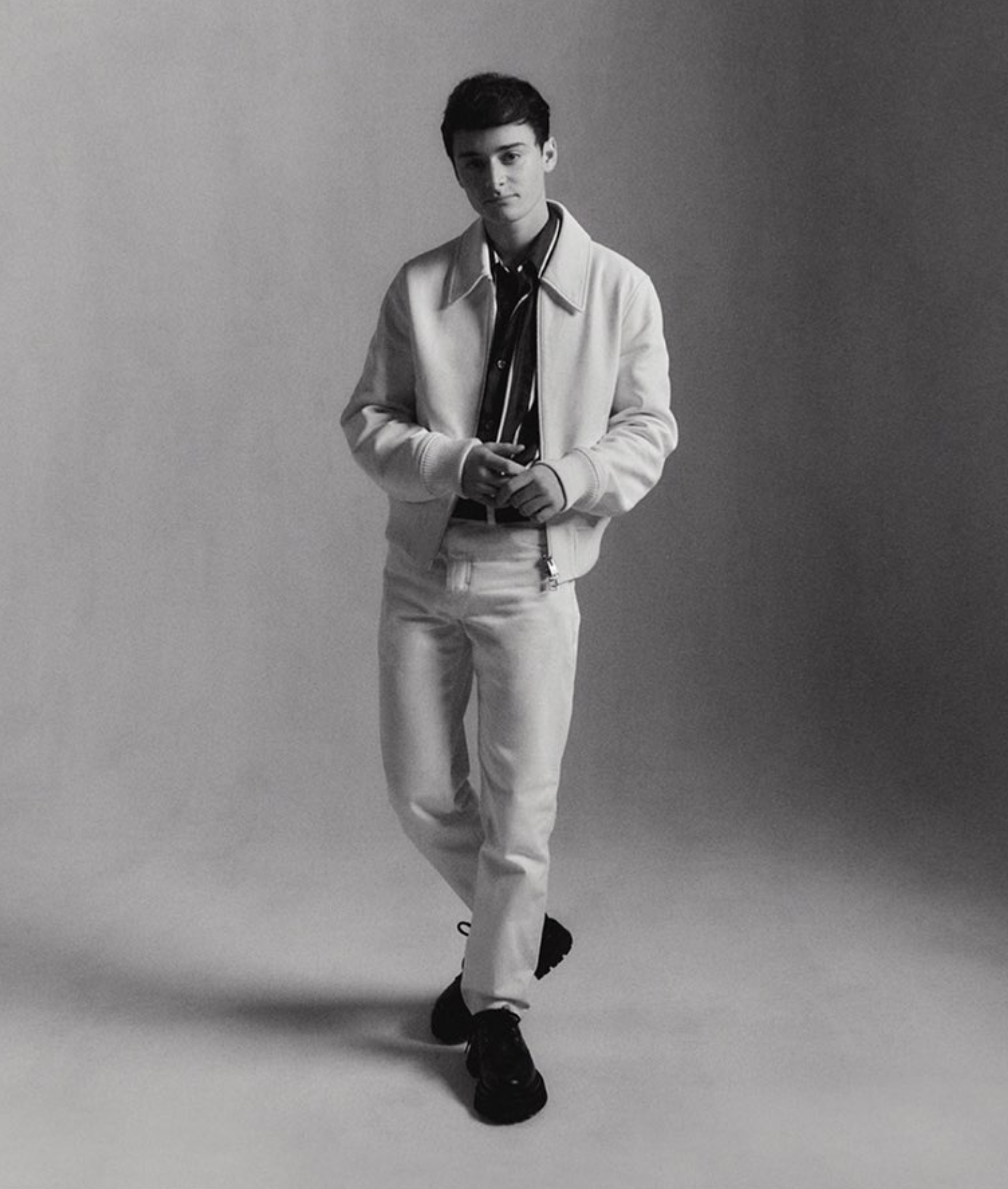 Full-length portrait of a young adult man in a white jacket and pants against a neutral backdrop, captured in a studio setting.