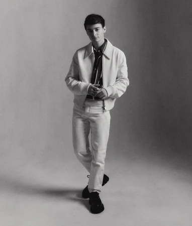Full-length portrait of a young adult man in a white jacket and pants against a neutral backdrop, captured in a studio setting.
