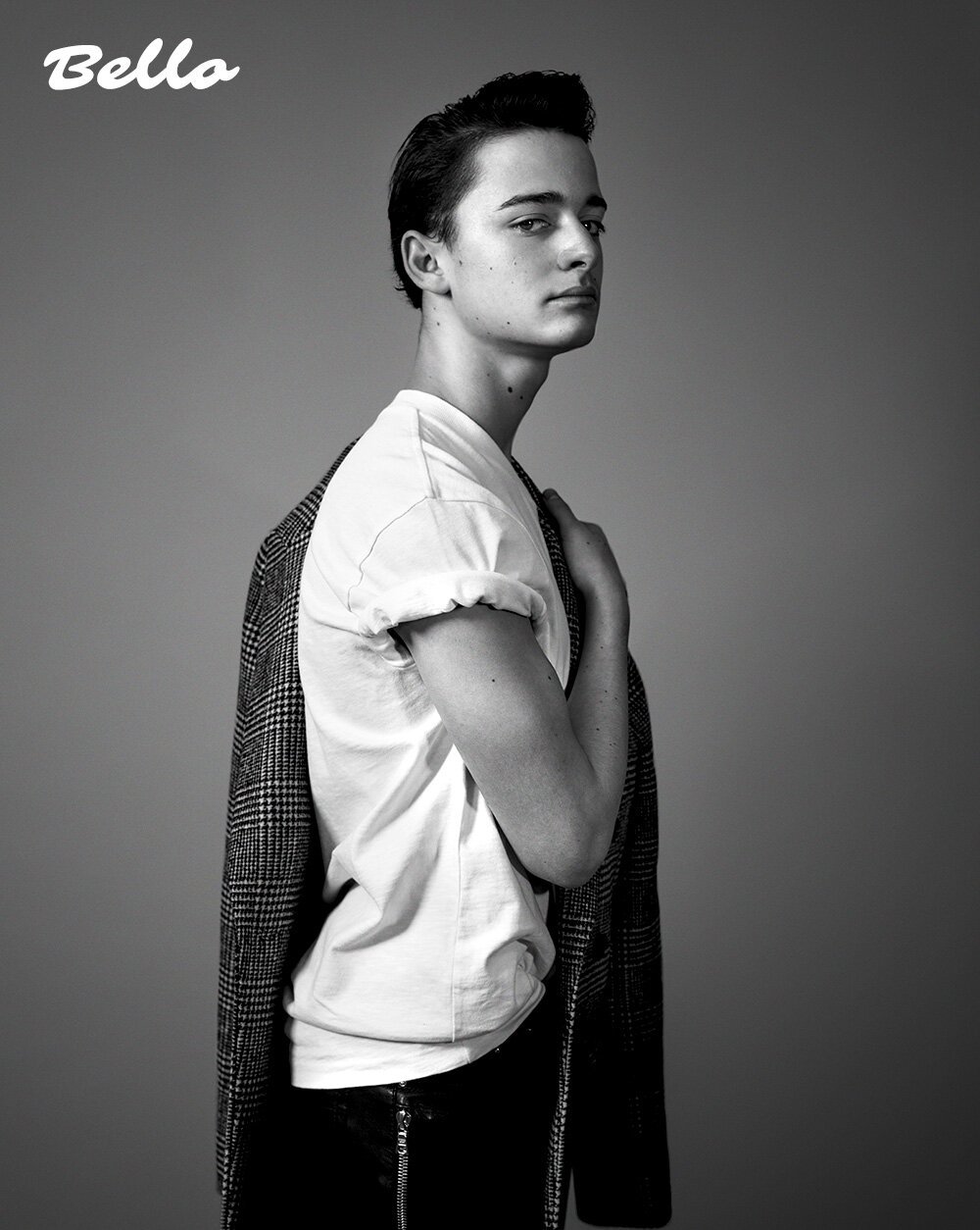 Monochrome portrait of young man in white t-shirt holding patterned jacket over shoulder, styled by Philippe Uter