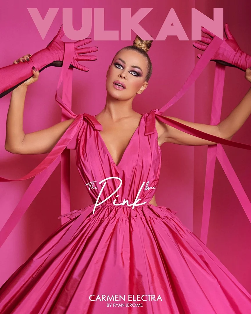 Carmen Electra fashion editorial: A blonde woman poses in a pink gown, accessorized with matching opera gloves and ribbons, against a pink background.