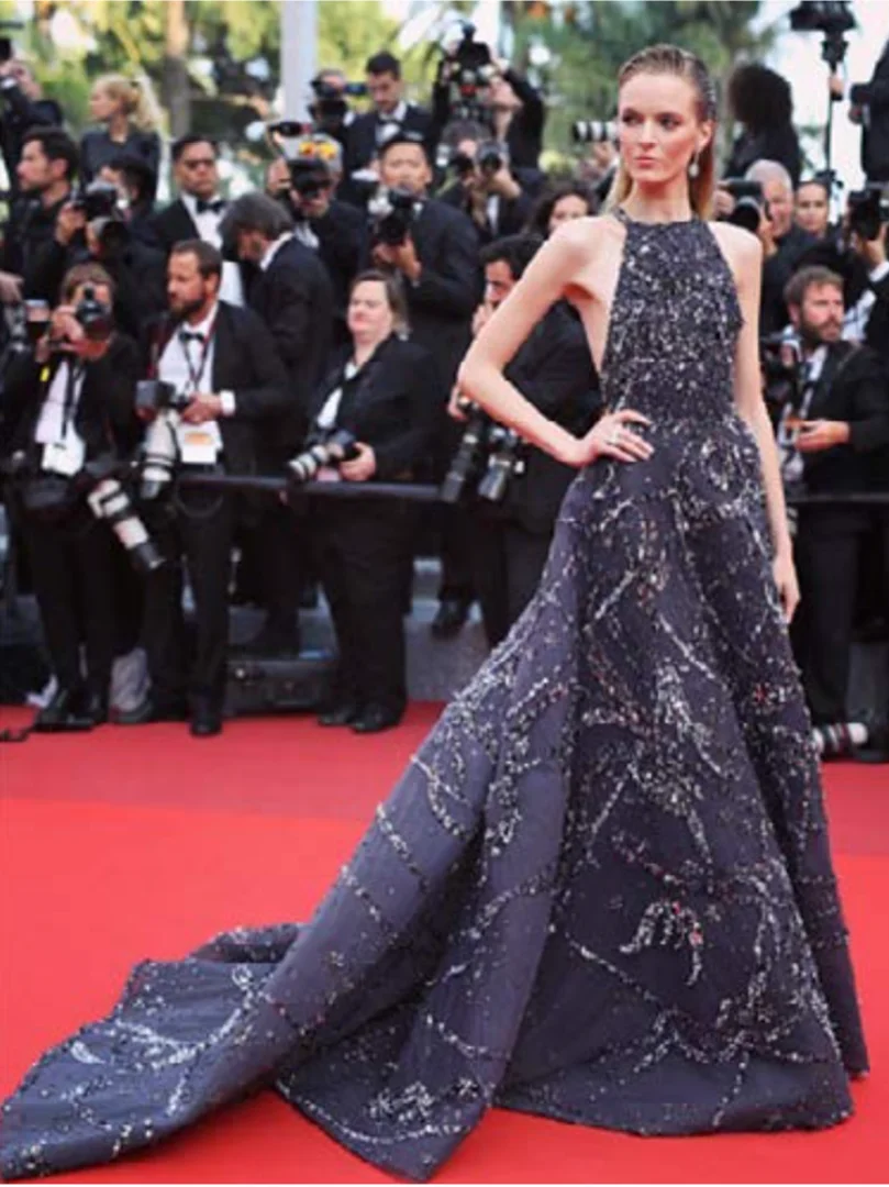 Woman in elegant gown poses on a red carpet in front of photographers at a public event, showcasing fashion and celebrity culture.