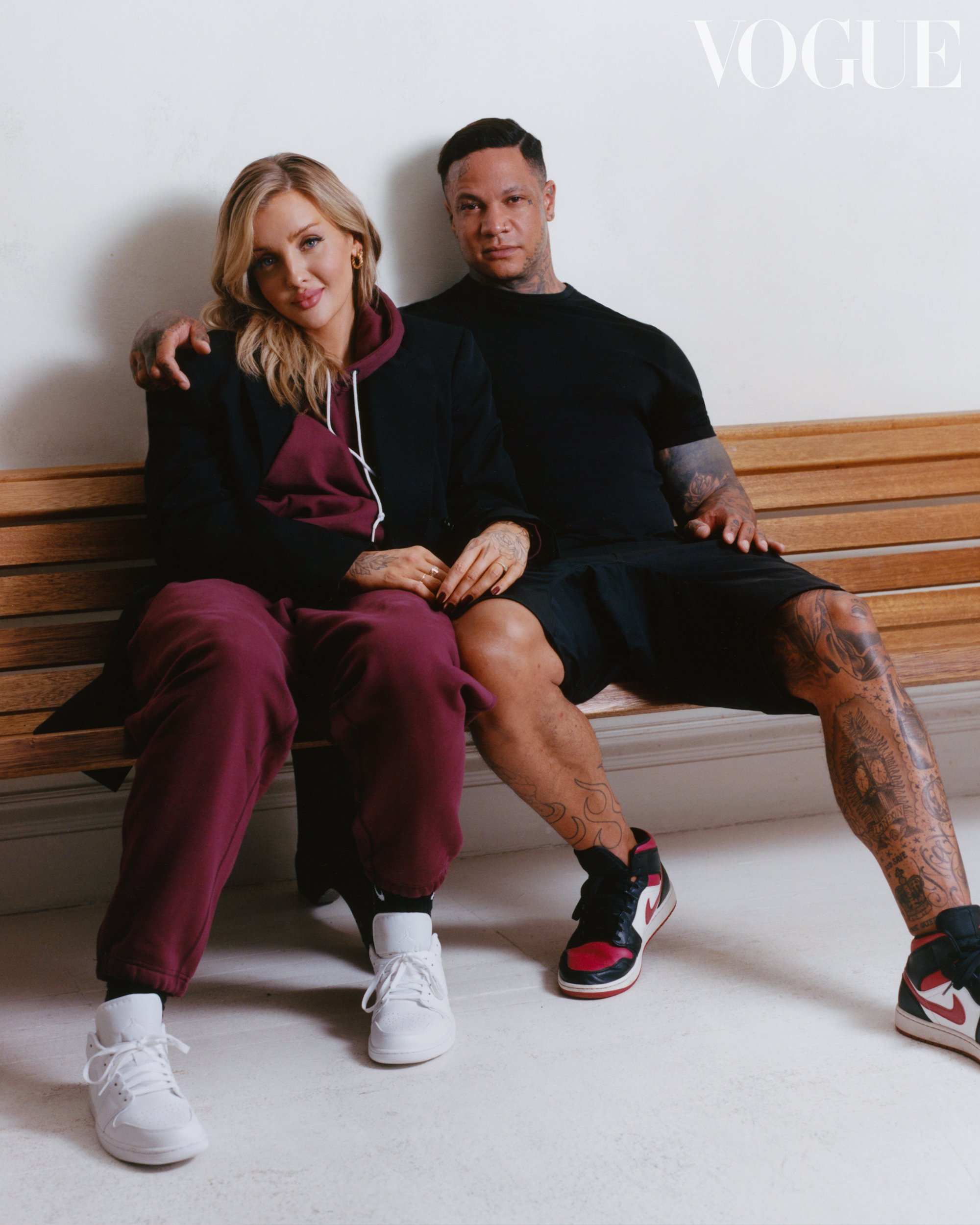 Fashion photo featuring a blonde woman and a man sitting on a bench. The woman is wearing a burgundy and black outfit, the man is in black.