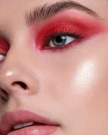 Extreme close-up portrait of a woman featuring bold red eyeshadow, defined brows, and glossy pink lips.