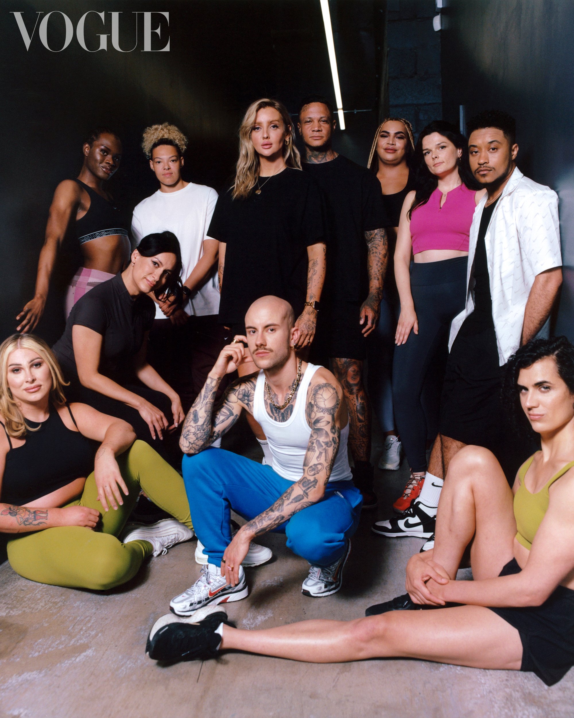 Diverse group poses in workout attire, captured indoors with concrete floors, against a dark wall, featuring a 'Vogue' logo.