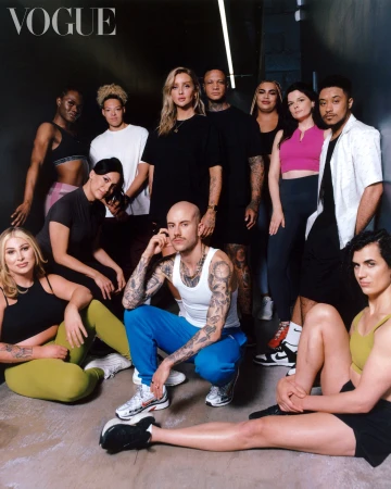 Diverse group poses in workout attire, captured indoors with concrete floors, against a dark wall, featuring a 'Vogue' logo.