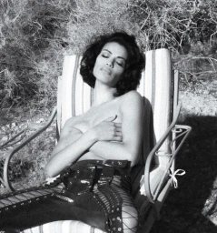 Monochrome portrait of a woman with dark hair reclining in a striped outdoor lounger wearing laced trousers