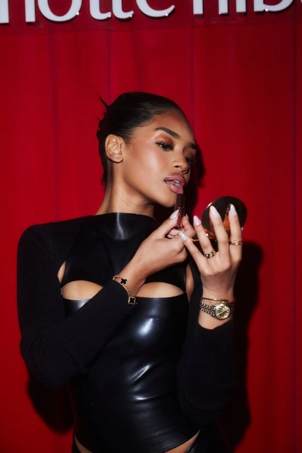 Woman applies lipstick in a close-up shot, wearing a black top against a red background with the Charlotte Tilbury logo visible.