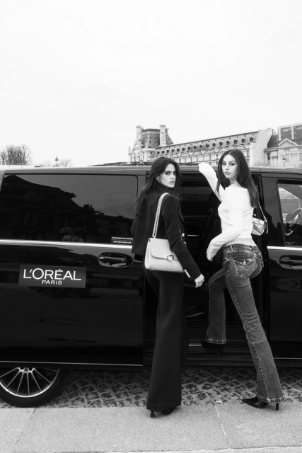 Two women exiting black car in black and white. One woman in denim, the other in tailored suit. Historic building in background.