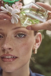 Close-up portrait of a woman with freckles holding a faceted perfume bottle near her face by Rebecca Spencer