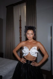 Woman wearing a strapless white bow top and black skirt with a large black hair bow standing indoors.