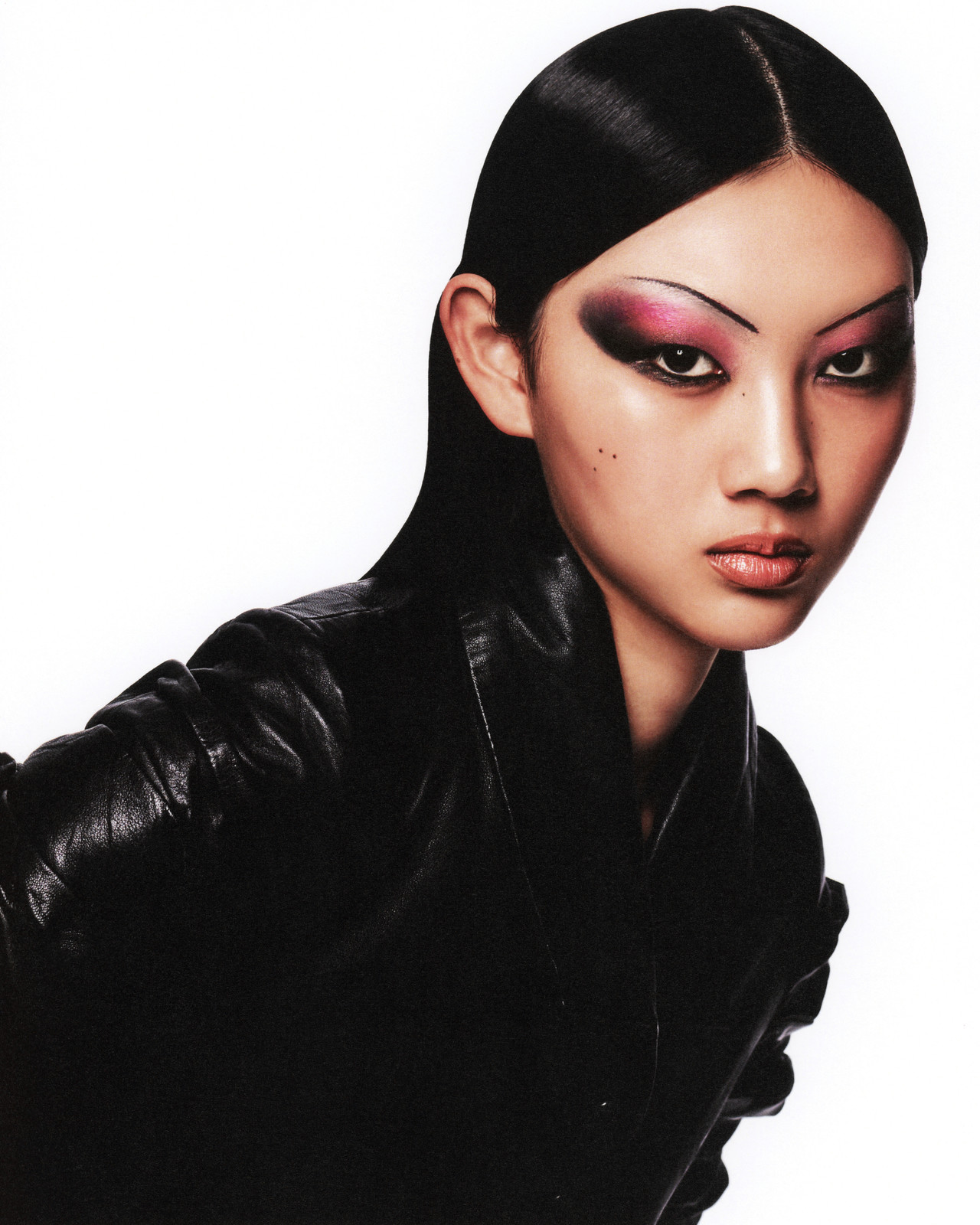 Striking portrait of an Asian woman with sleek black hair and dramatic magenta eyeshadow, wearing a black leather jacket against a white backdrop.
