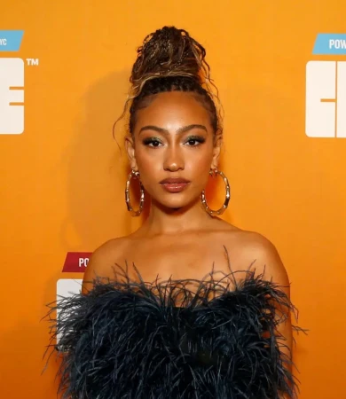 Portrait of a stylish young woman with updo, hoop earrings, and a black feather dress against an orange background.